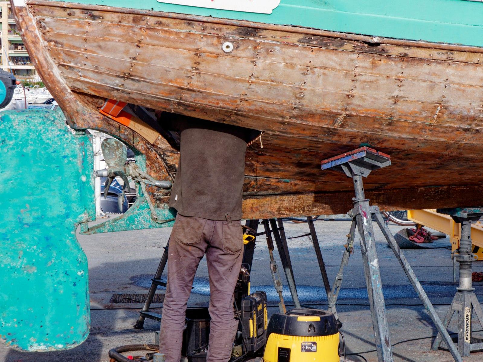 Une personne travaille sous la coque d'un bateau en bois posé sur béquilles, au Vieux-Port de Marseille