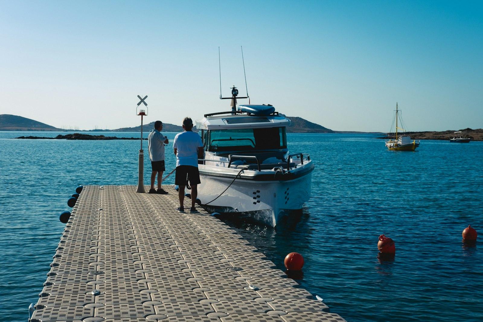 Deux plaisanciers sur un ponton flottant, à côté d'un bateau à moteur amarré dans une baie