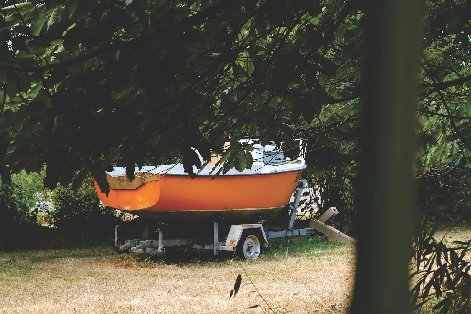 Petit bateau à coque orange posé sur sa remorque dans un jardin du Finistère, entre les arbres